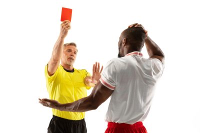 Referee showing a red card to a displeased african-american football or soccer player while gaming isolated on white background. Concept of sport, rules violation, controversial issues, emotions.